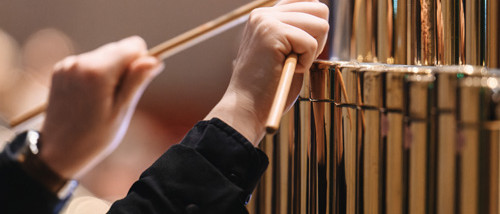 Photo d'un gros plan sur des mains qui tiennent des baguettes et tapent sur des cloches tubulaires